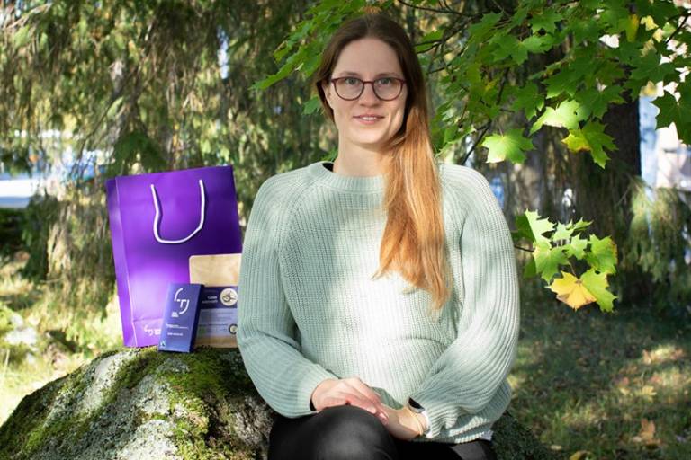 Pitkätukkainen nainen istuu kivellä vieressään erilaisia pakkauksia.