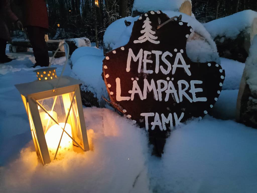 Kyltti Metsälämpäreestä ja vieressä lyhty lumihangessa