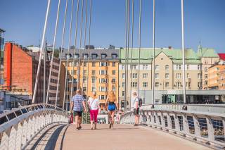 Four people walking on Laukontori bridge, colourful houses on the background. 