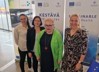 Neljä naista Kestävä aivoterveys -hankkeen rollupin edessä.