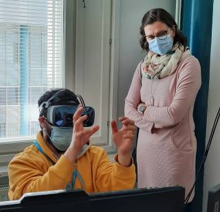 Mies VR-lasit päässä, nainen tarkkailee taustalla.