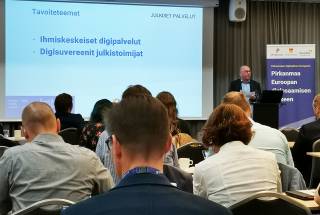 Ihmisiä luentosalissa, esityksenpitäjän dia näkyvissä.