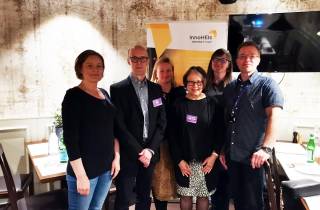 Iloinen kuuden hengen ryhmä, taustalla keltainen rollup.