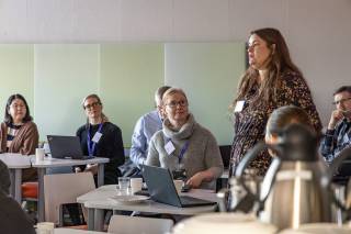 Brown-haired woman standing and explaining to others in a classroom.
