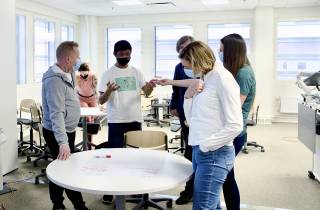 Henkilöt pöydän ympärillä keskustelemassa.