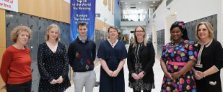 A group of seven persons standing in the corridor and smiling