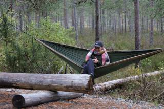 Nainen istuu puiden väliin viritetyssä riippumatossa