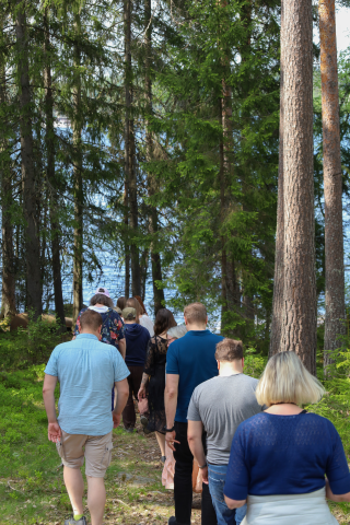 Seminaarin osallistujat kulkevat jonossa metsäpolulla, taustalla järvimaisema