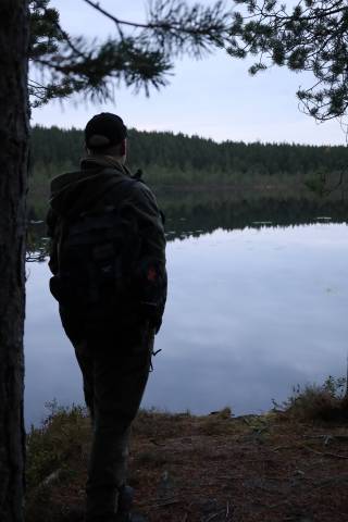 Henkilö katselee lammelle puuhun nojaten