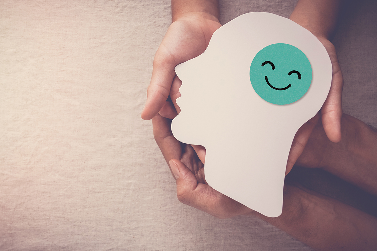 Kädet pitelevät pahvista hmisen pään kuvaa. Aivojen kohdalla hymynaama.