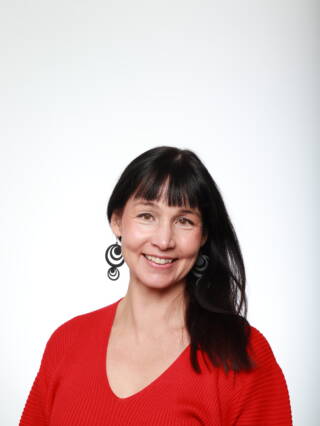 Tummahiuksinen nainen (Liisa Mustanoja) hymyilee kameralle.