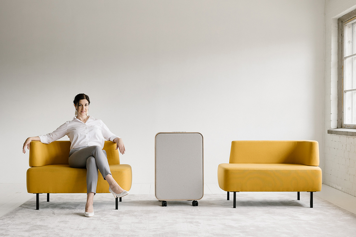 Tummatukkainen nainen istuu keltaisella nojatuolilla vaaleassa tilassa.