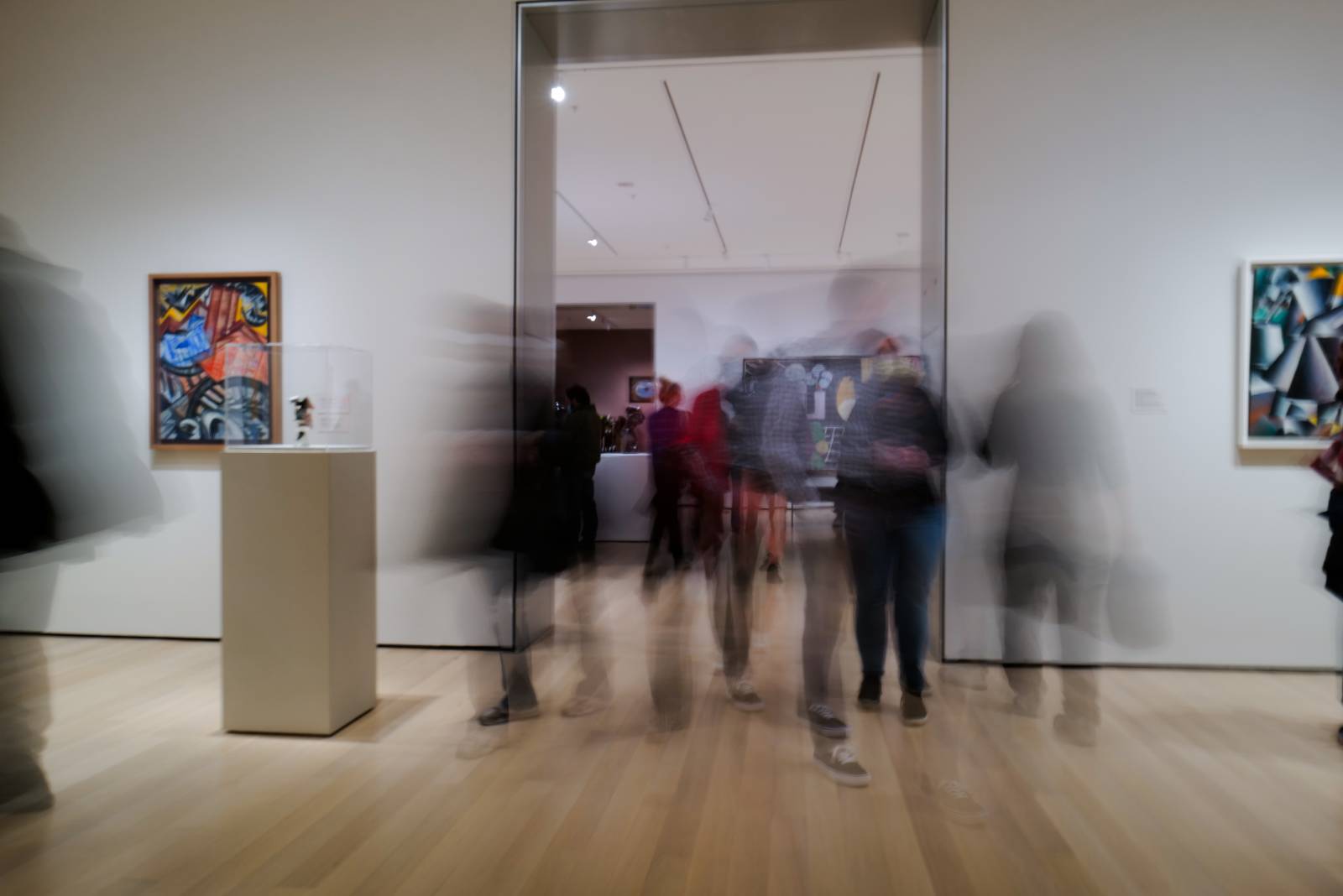 Kuva, jossa on joukko tarkentumattomia ihmishahmoja taidenäyttelyssä