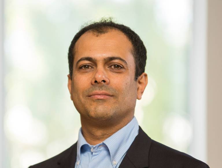 Hymyilevä tummatukkainen mies puvuntakissa.