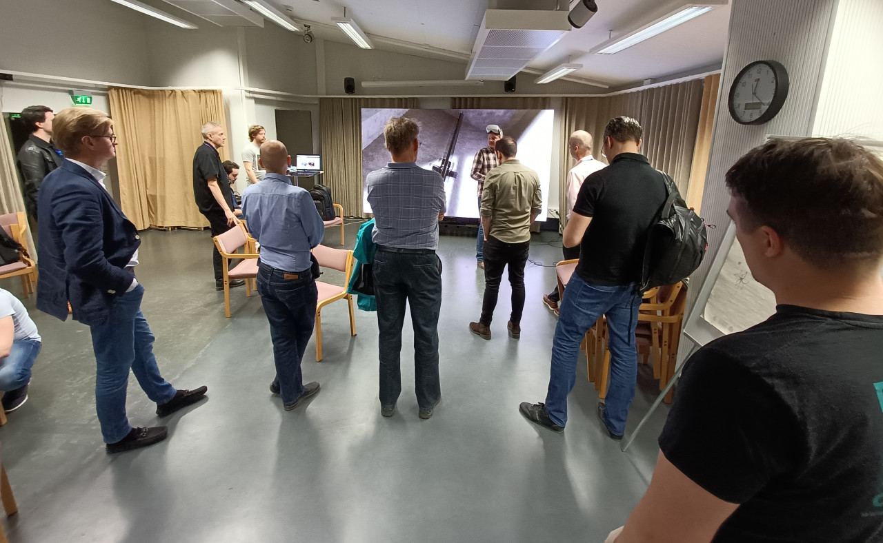 A group of men is standing in a room and following a presentation.
