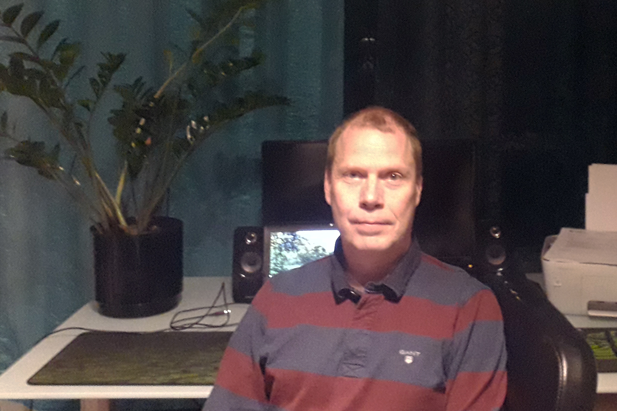 Mies istuu työpöydän ääressä taustalla viherkasvi ja tietokone.