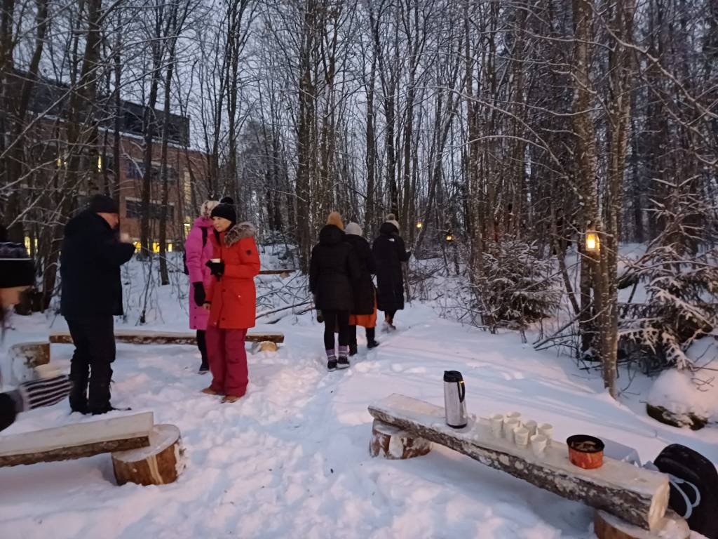 Avajaisväkeä suuntaamassa lumista polkua pitkin metsikköön glögimukien kanssa