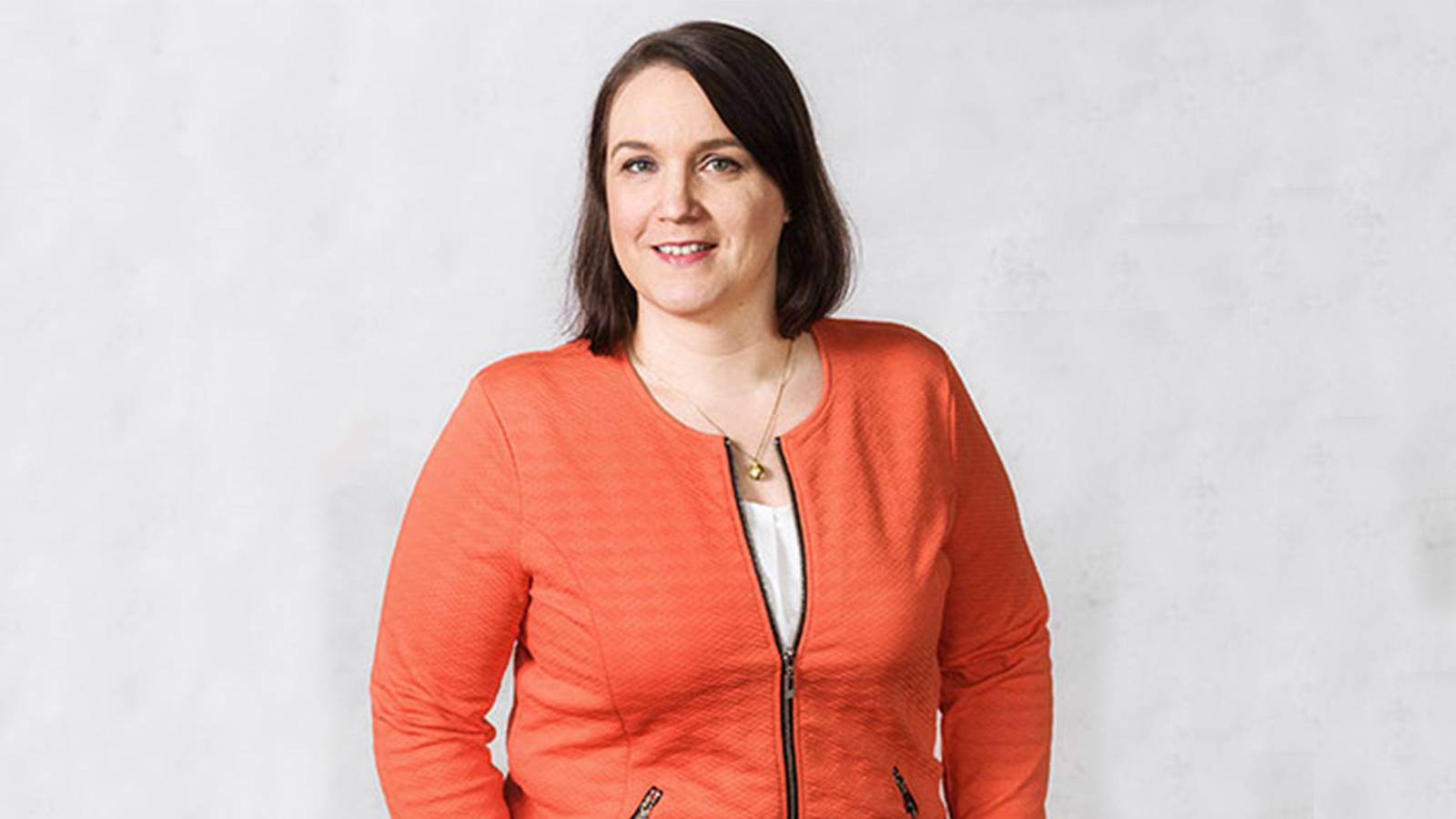 Tummatukkainen nainen oranssissa villatakissa.