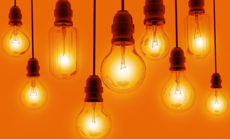 Oranssilla seinällä roikkuu eritasoisessa rivissä hehkulamppuja, joissa on valo.
