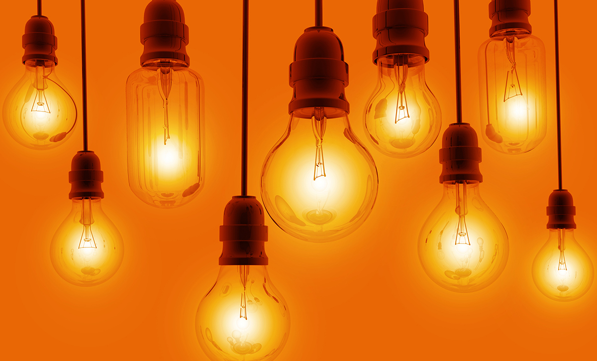 Oranssilla seinällä roikkuu eritasoisessa rivissä hehkulamppuja, joissa on valo.