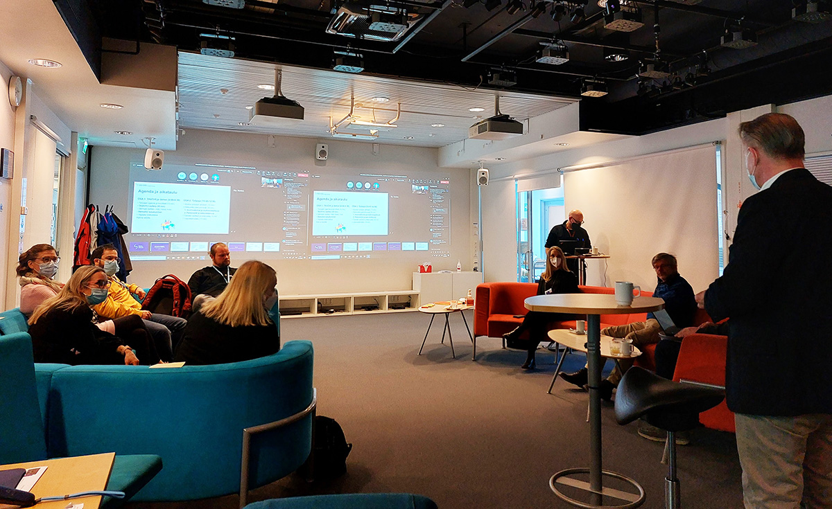 Ihmisiä neuvottelutilassa, seinille heijastettu esitys.