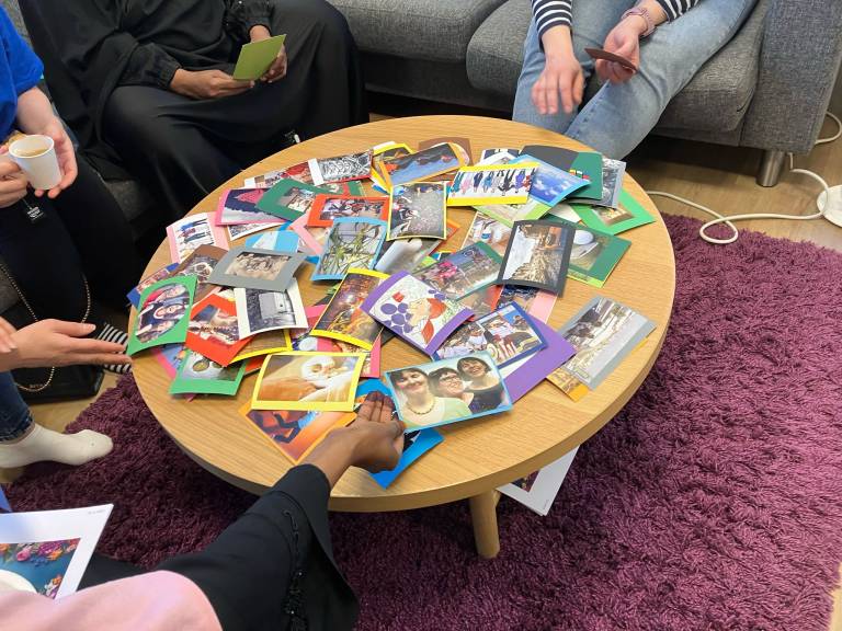 Pöytä, jossa on paljon kortteja erilaisilla kuvilla sekä henkilöitä istumassa pöydän ääressä.