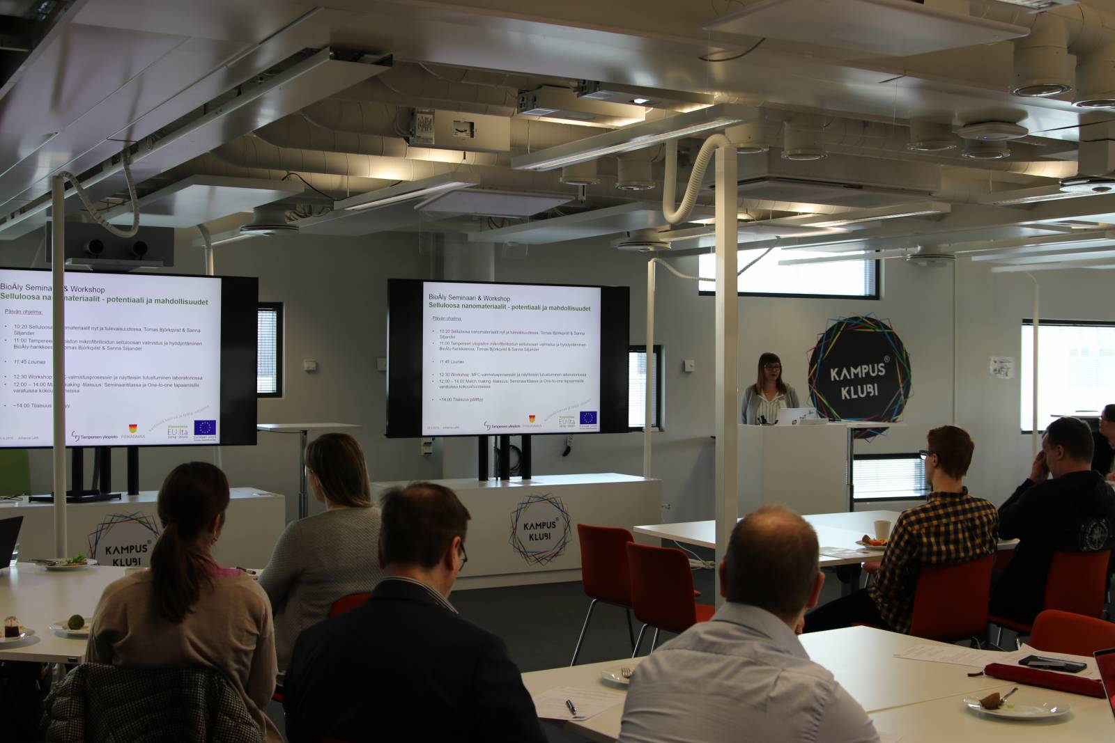 Ihmisiä selin kameraan seminaatilassa. Projektikoordinaattori Johanna Lahti pitää esiltelmää