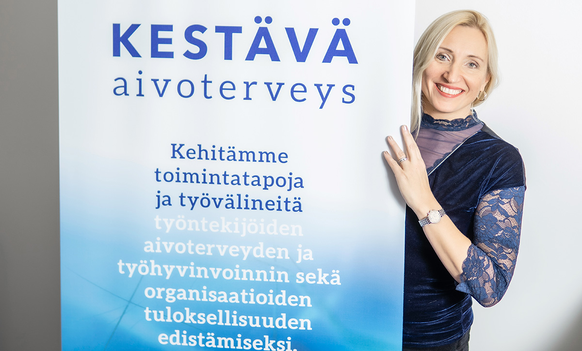 Hymyilevä Kaisa Hartikainen kurkistaa rollupin takaa.