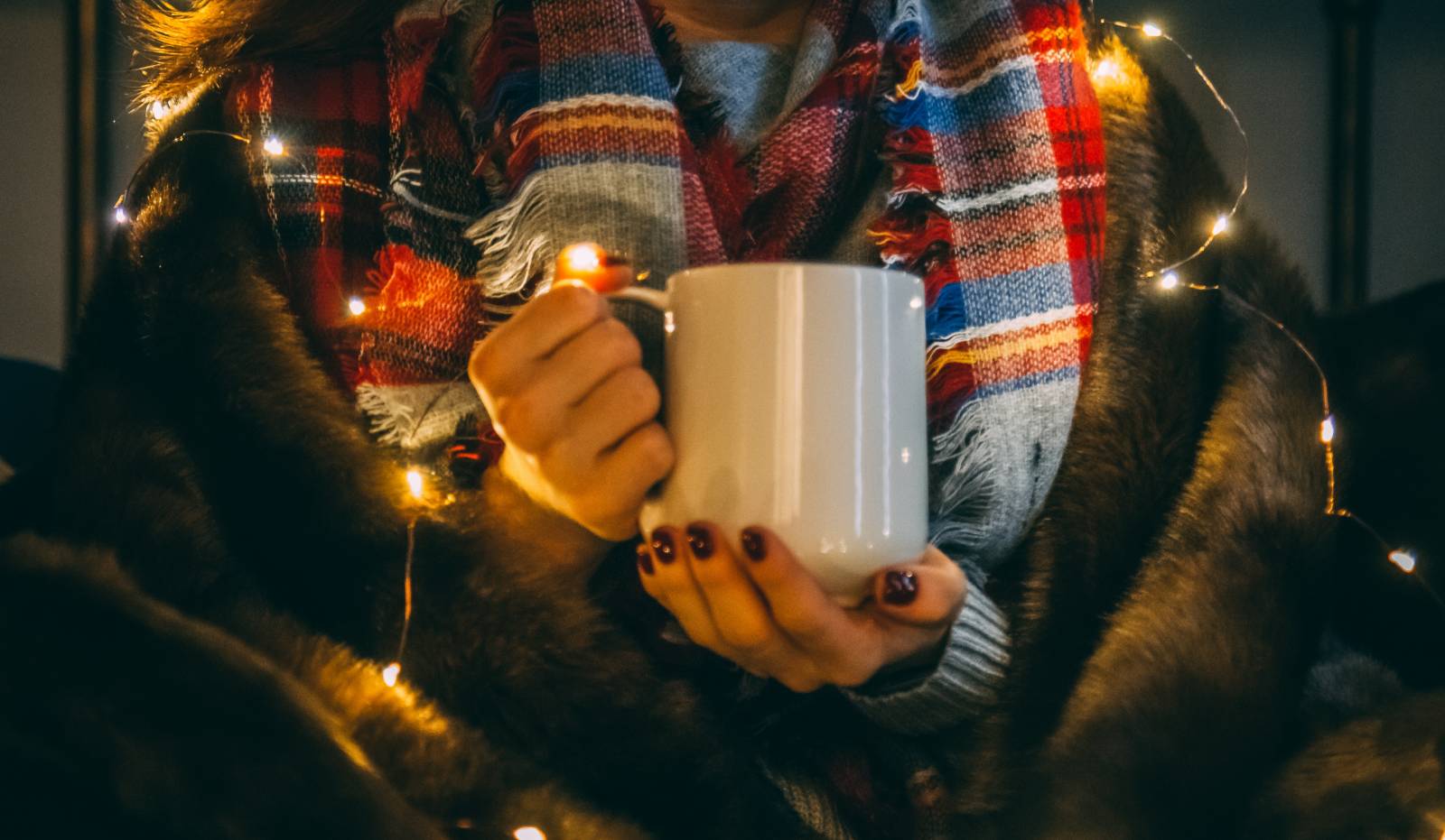 Kuvituskuva. Vilttiin kääriytynyt nainen pitelee mukia käsissään.