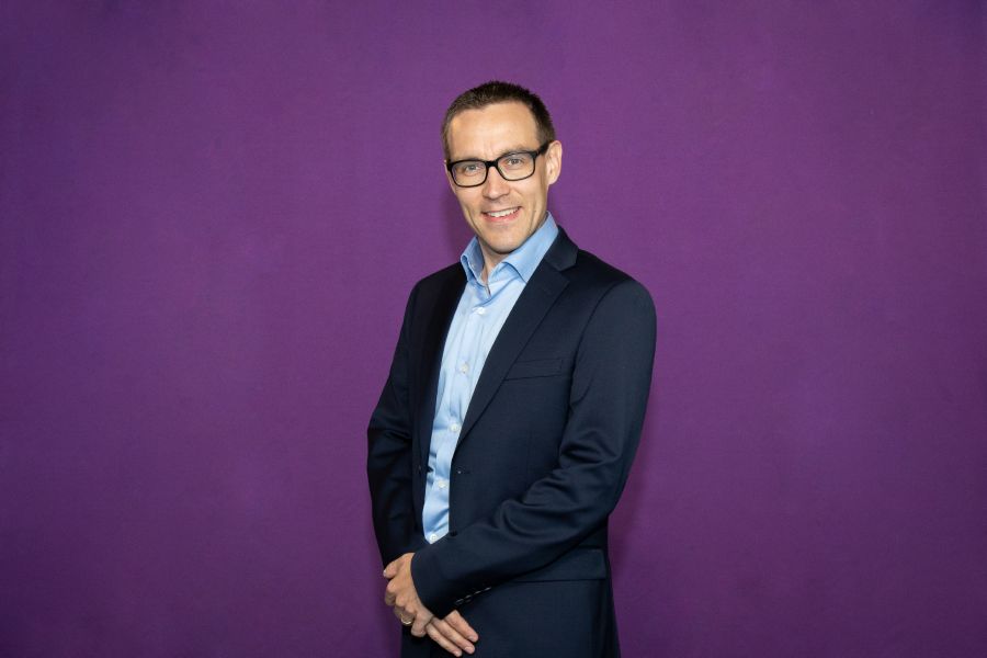 Tummatukkainen mies tummassa puvussa.