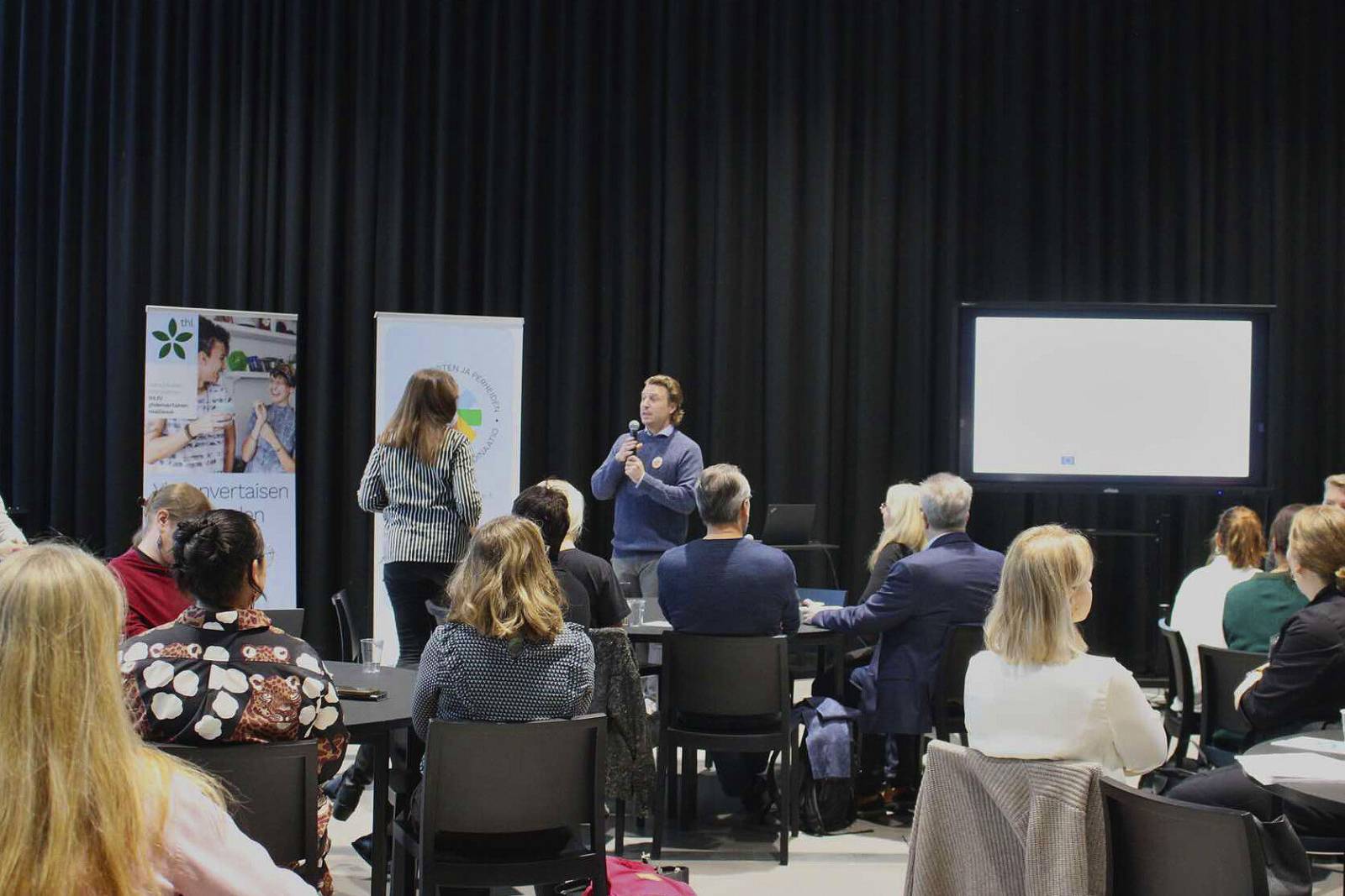 Tilaisuus, jossa edessä puhuja ja kuuntelijoita.