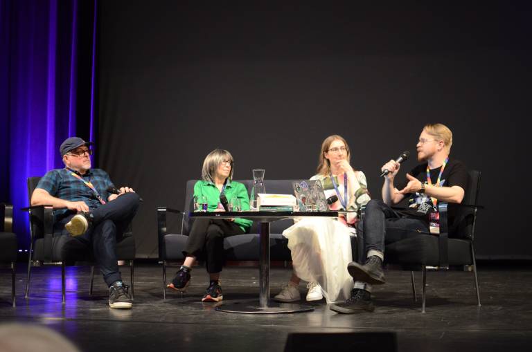 Valokuva, jossa vasemmalta alkaen Jeff VanderMeer, Ann VanderMeer, Emmi Itäranta ja Esko Suoranta ovat esiintymislavalla keskustelemassa. Esko puhuu mikrofoniin.