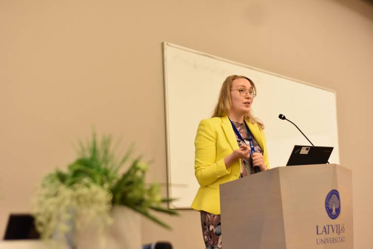 Vilma Wacklin keltaisessa jakussa pitämässä esitelmää.