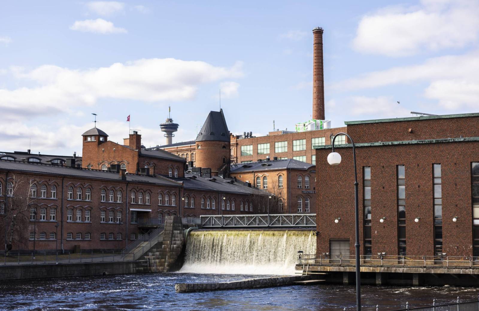 Keskellä Tammerkoski, jonka sivuilla on punatiilisiä tehdasrakennuksia. Taustalla tehtaan piippu ja Näsinneula.