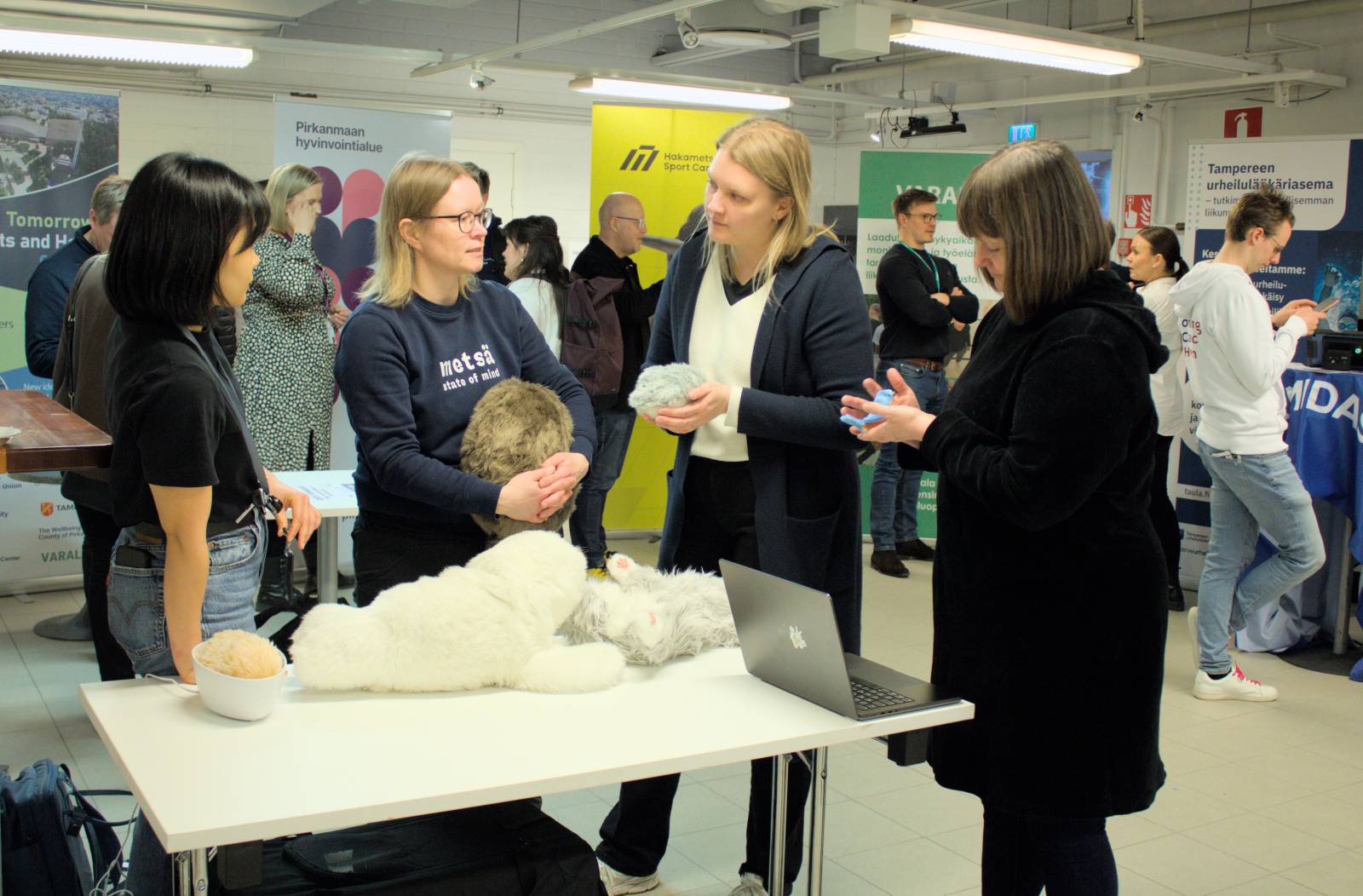 Ryhmä ihmisiä keskustelee pöydän äärellä, pöydällä useita robottieläimiä ja kannettava tietokone.