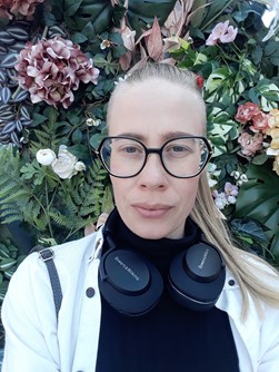 Kuvassa on hankkeen tutkija Ella Poutiainen. Poutiainen katsoo kameraan, taustallaan vihreää kasvillisuutta ja kukkia.