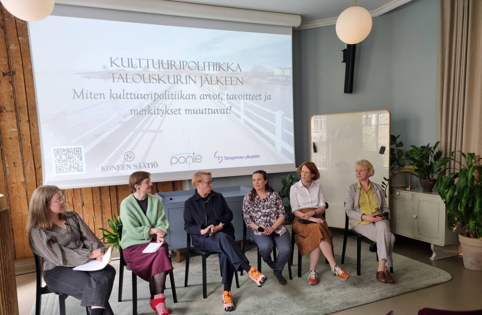 Kuusi panelistia istumassa rivissä ja keskustelamassa. Taustalla valkokangas, jossa teksti: Kulttuuripolitiikka talouskurin jälkeen: miten kulttuuripolitiikan arvot, tavoitteet ja merkitykset muuttuvat?
