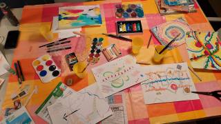Photo of watercolours, acrylic paints, and newspaper cutouts on a table