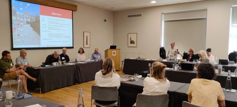 Photo of conference, Johanna and other scholars sitting at tables.