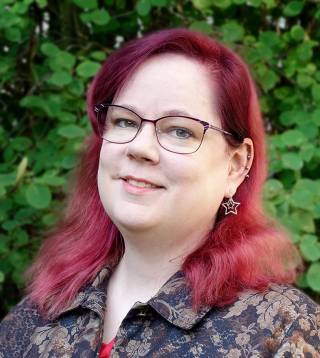 A woman with dyed red hair and glasses smiling slightly.