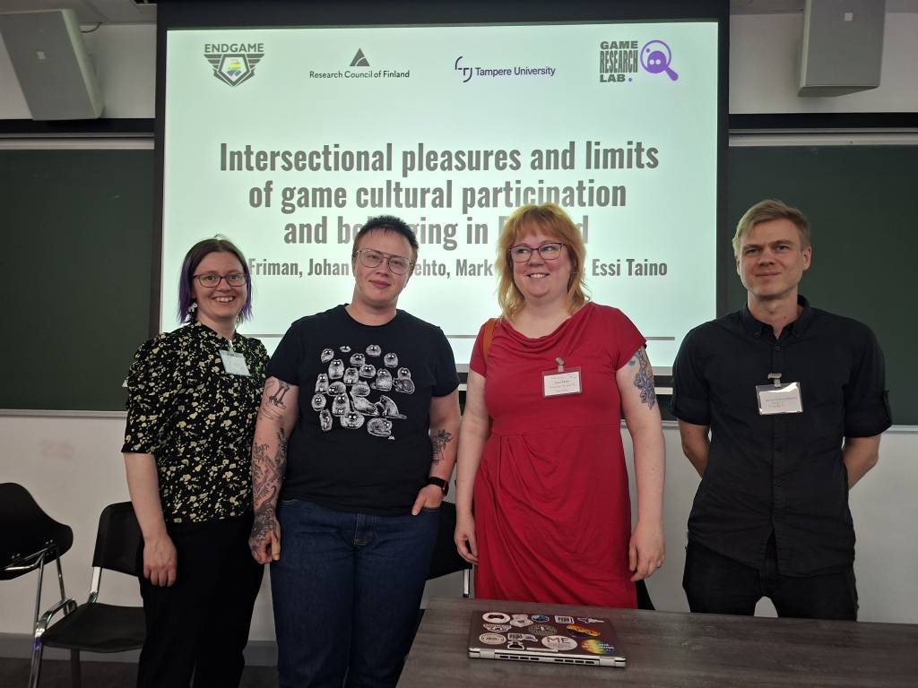 Project's researcher team standing in front of a screen displaying their presentation title at DiGRA 2026