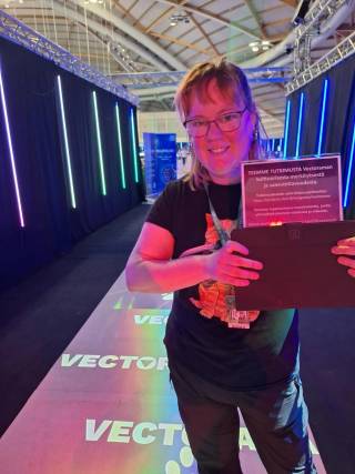 A smiling researcher standing on a mat decorated with Vectorama logos, presenting a research information sheet to the camera.