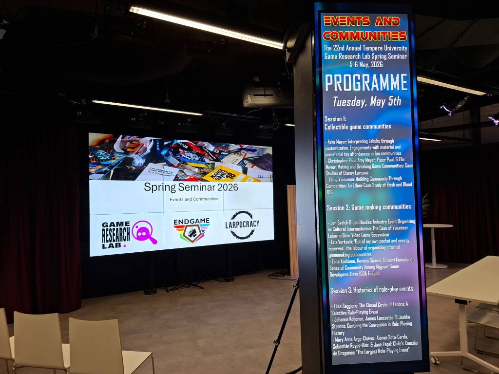Photo of two screens. On the left, screen displaying the spring seminar 2026 title and sponsor logos. On the right, a screen displaying the event programme.