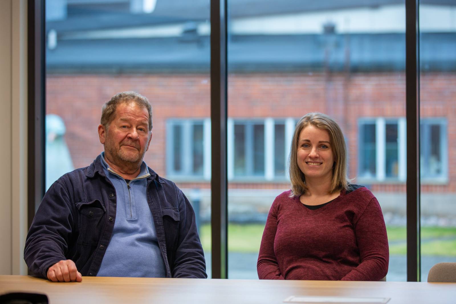 Kuvassa istuu kaksi ihmistä pyödän ääressä. Molemmat hymyilevät.