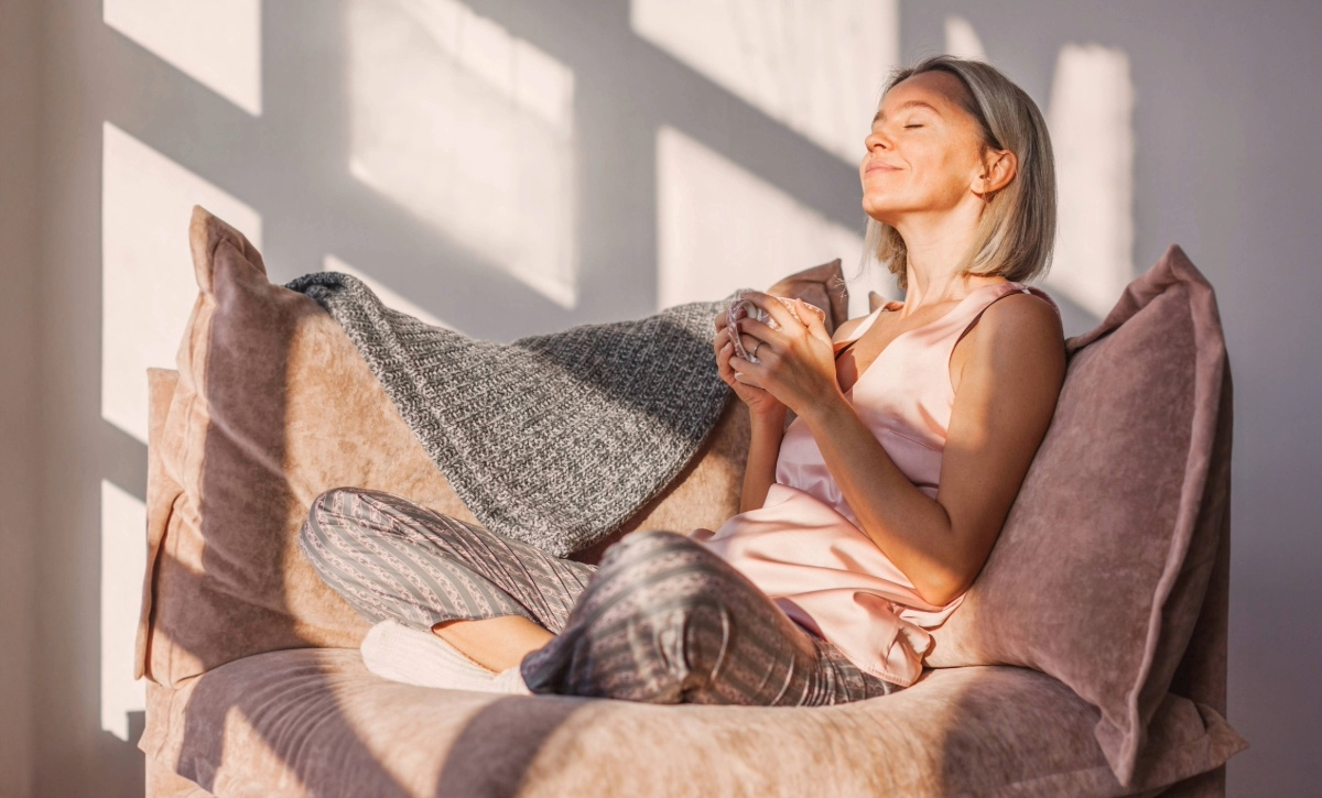 Keski-ikäinen henkilö istuu tuolissa kahvikuppi kädessä silmät kiinni ja hymyilee