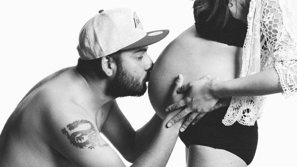 Oletettu isä suutelee raskaana olevan vatsaa.