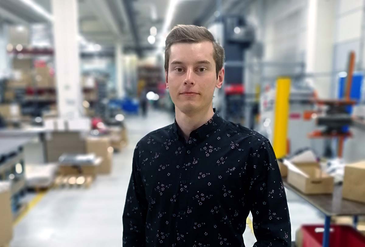 Mustaan paitaan pukeutunut nuori mies tehdashallissa.
