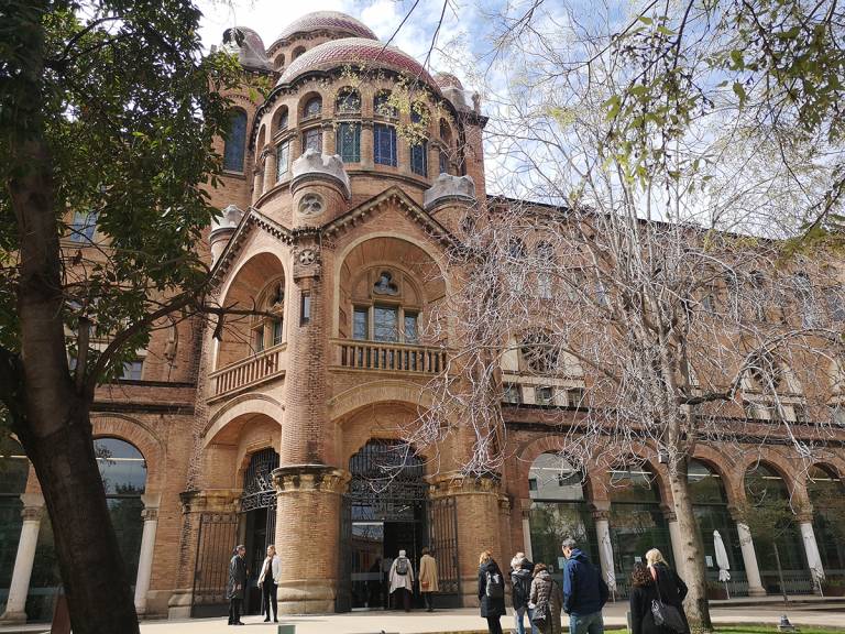 Vanha historiallinen rakennus Barcelonassa, etu-alalla ihmisiä ja puita.