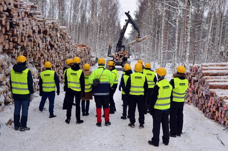 People in a wintery forest looking at operating forest machinery.