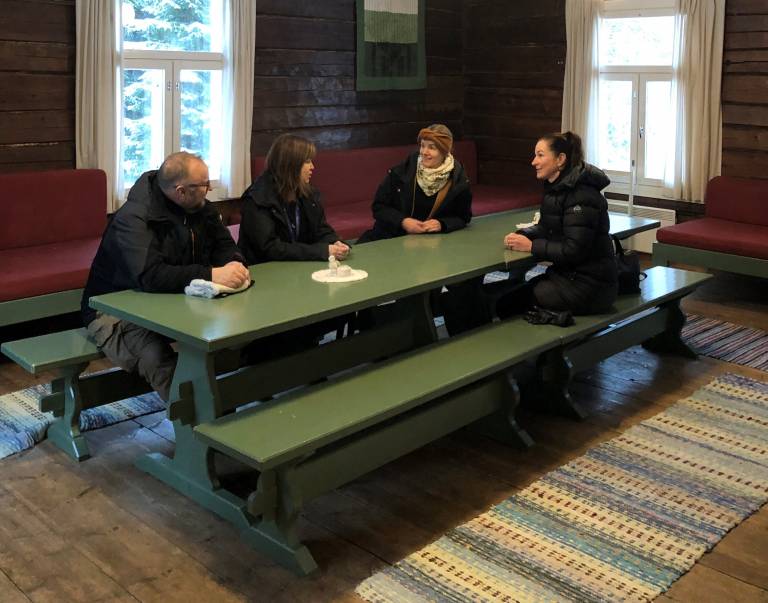 Neljä henkilöä vanhan hirsitalon olohuoneessa suuren vihreän pöydän ympärillä Kintulammilla.